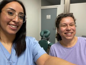 Une soignante en blouse bleue prend un selfie avec Aurélie. Elles sont souriantes, entre elles ont peut voir le fauteuil de massage Amma assis.